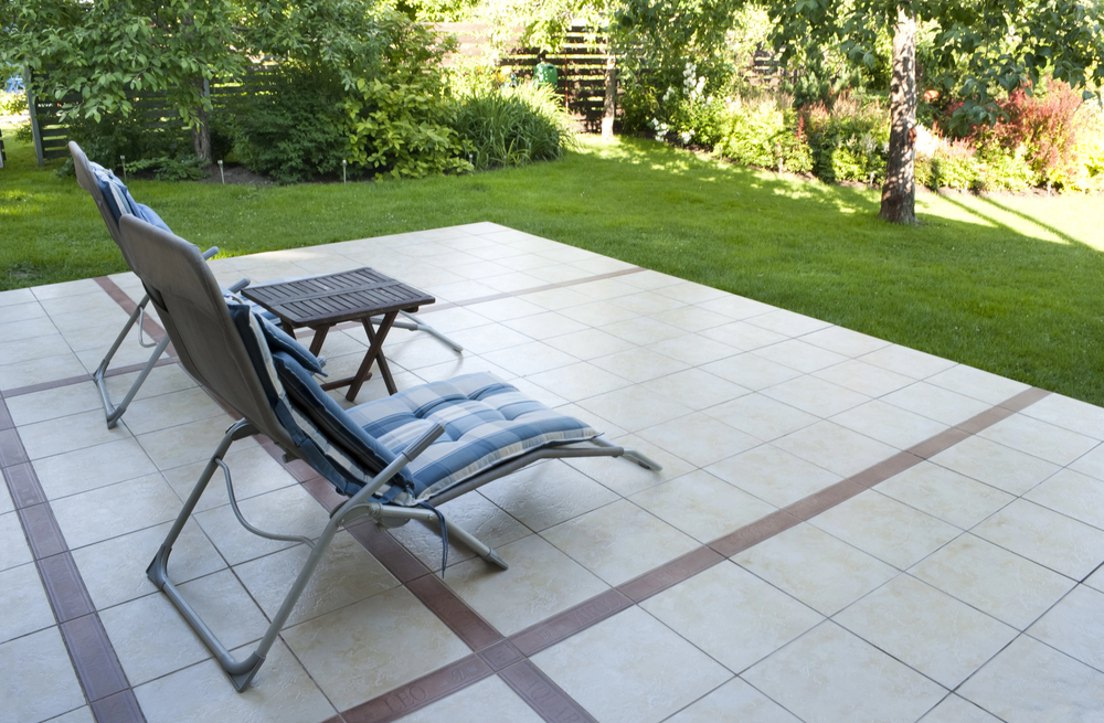 Terrasse carrelée en dalles claires avec frise contrastée au bord d’un jardin